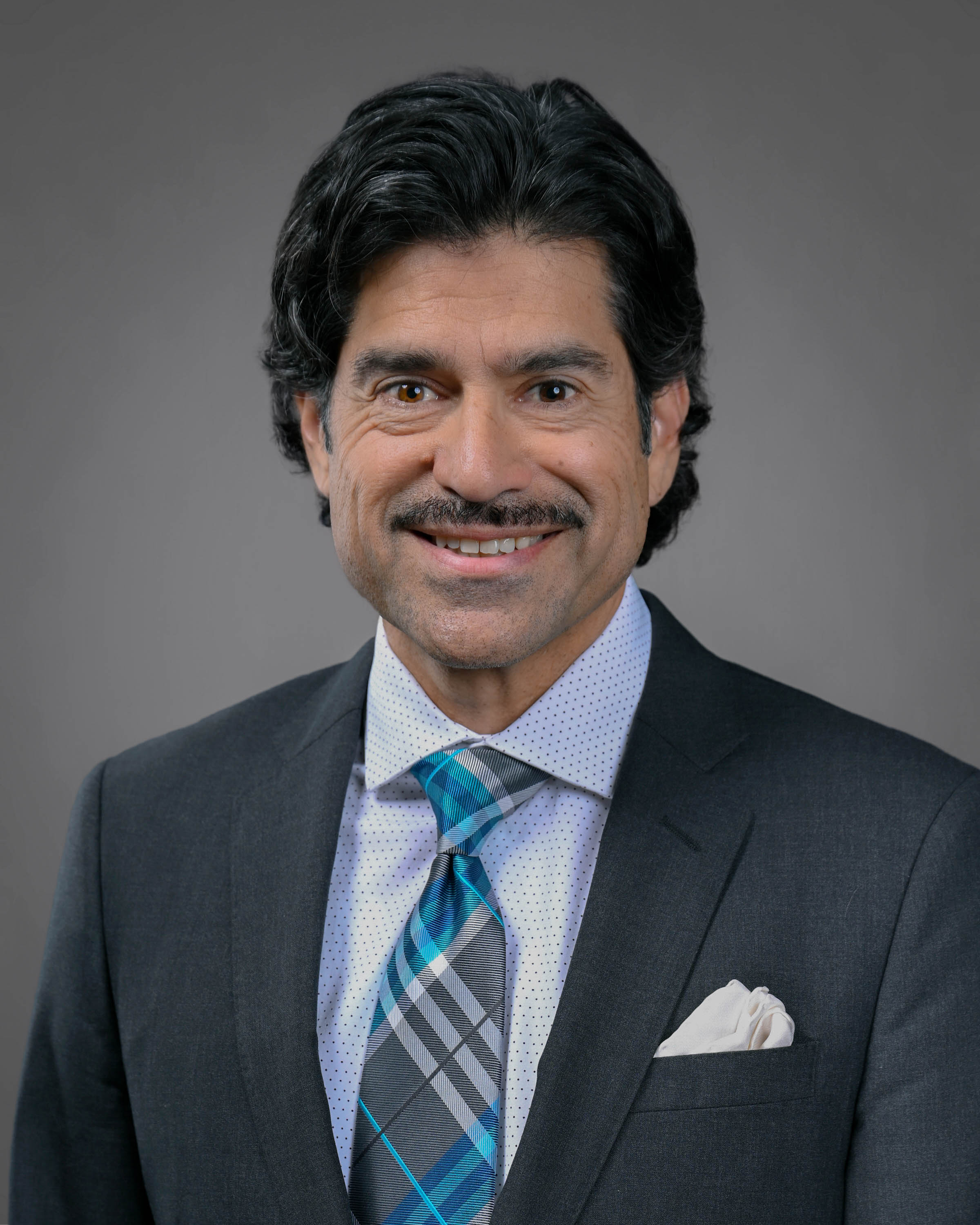 Smiling man with dark hair and a mustache in a dark grey suit with a shit and tie.